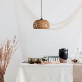 Esstisch mit Dekoration, hängende Korblampe, Vase, Gläser und getrocknete Pflanzen in modernem Raum.