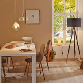 Esszimmer mit weißem Tisch, braunen Stühlen und Stehlampe vor hellem Fenster. Hängelampen und Wandbild ergänzen das Ambiente.