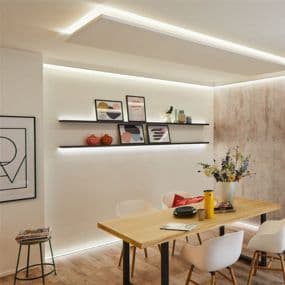 Modernes Esszimmer mit Holz-Tisch, weißen Stühlen, Wandregalen und LED-Beleuchtung. Kunstwerke und Deko auf Regalen.