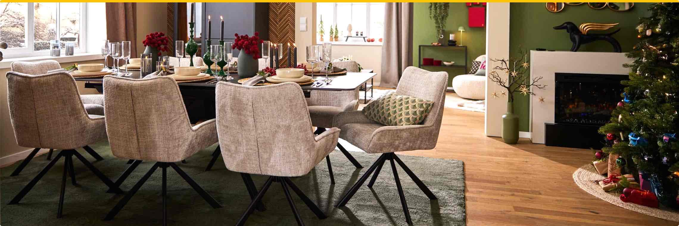 Weihnachtlich dekoriertes Esszimmer mit gedecktem Tisch, gemütlichen Stühlen und Weihnachtsbaum neben dem Kamin.