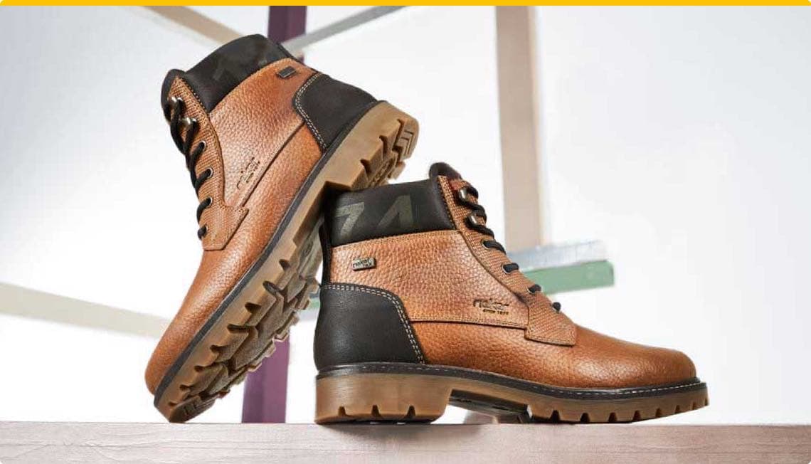 Zwei braune Herrenstiefel mit schwarzem Bereich an der Ferse und robusten Sohlen auf einem hellen Hintergrund.