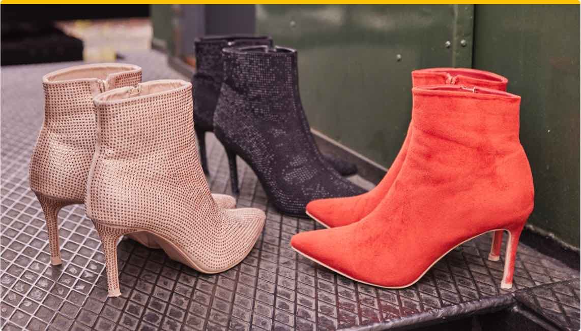 Drei Paar Stiefeletten – beige, schwarze und rote Stiefeletten mit Absatz auf Metallgitterboden nebeneinander angeordnet