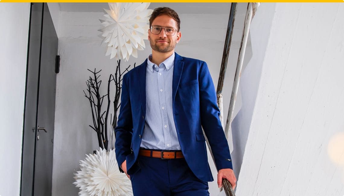 Mann in blauem Anzug und gestreiftem Hemd steht auf Treppe, im Hintergrund moderne weiße Dekorationen