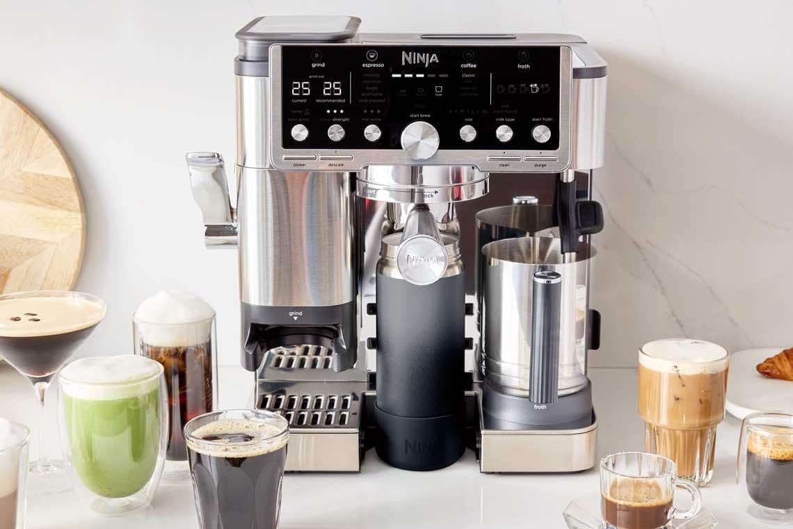 Vielseitige Kaffeemaschine von Ninja, umgeben von verschiedenen Kaffeegetränken und einem Croissant auf einem Teller.