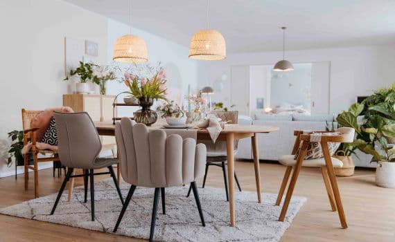 Gemütliches Esszimmer mit Holztisch, verschiedenen Stühlen, Blumenstrauß und Hängelampen auf Teppich.