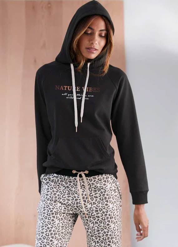 Person in schwarzem Hoodie mit Aufschrift "Nature Vibes" und gemusterter Jogginghose.
