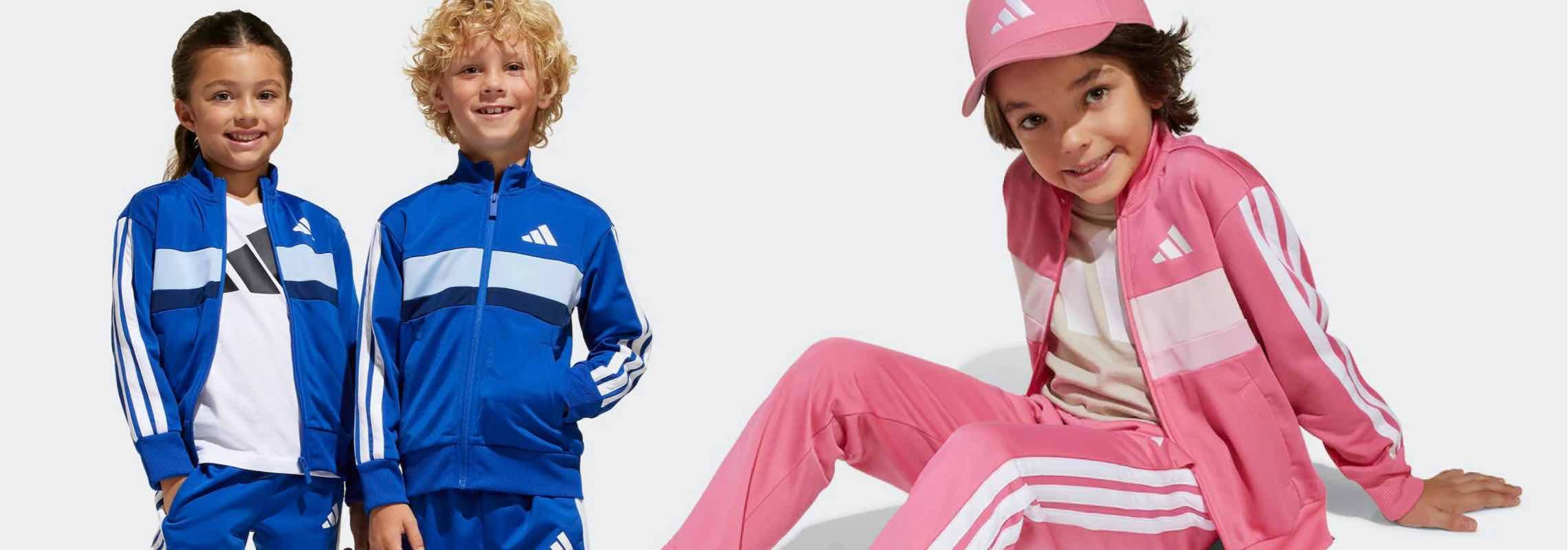 Drei Kinder in Adidas-Trainingsanzügen, zwei in Blau, eins in Pink, posieren lässig.