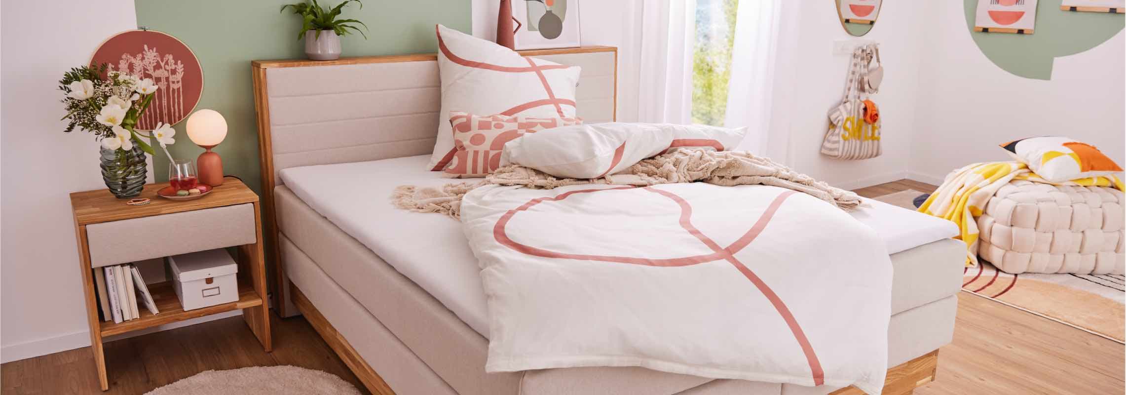 Modernes Schlafzimmer mit beigem Bett, Nachttisch, Blumenstrauß und gemütlicher Dekoration, helle und einladende Atmosphäre.