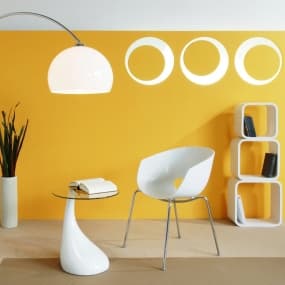 Modernes Wohnzimmer mit gelber Wand, weißem Stuhl, Glastisch, Bogenlampe und Pflanze in Vase.