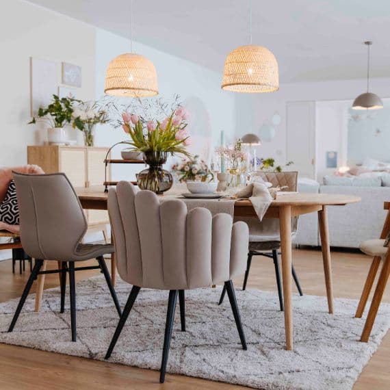 Esszimmer mit Holztisch, gepolsterten Stühlen und Blumenvasen, zwei geflochtene Lampen hängen über dem Tisch