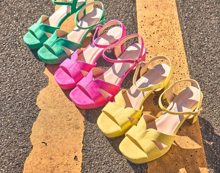 Farbenfrohe Sandaletten in Grün, Pink und Gelb auf Asphalt mit gelber Linie.