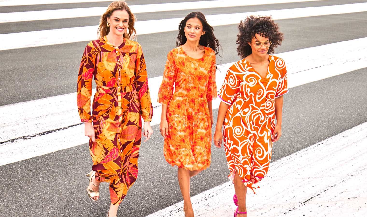 Drei Frauen in orangefarbenen Kleidern gehen auf einer Straße.