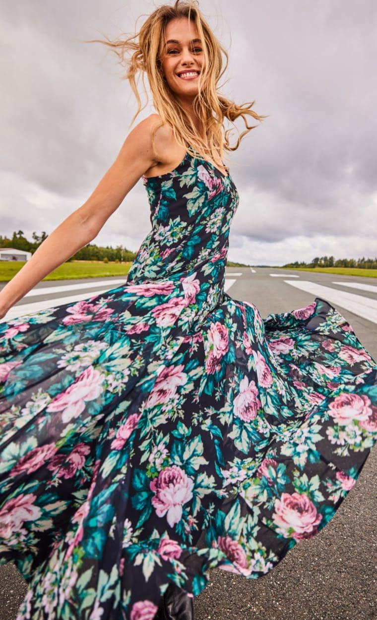 Frau in einem geblümten Kleid tanzt auf einer Landebahn, ihr Kleid weht im Wind.