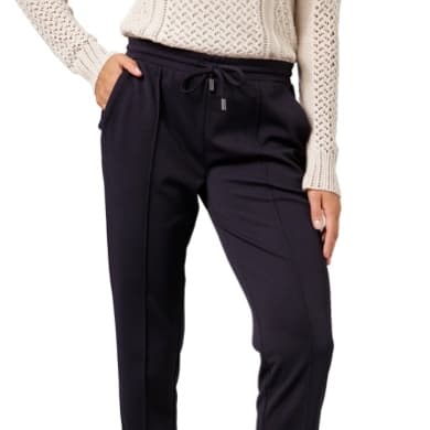 Frau trägt eine dunkelblaue Jogginghose und einen cremefarbenen Strickpullover, eine Hand in der Tasche