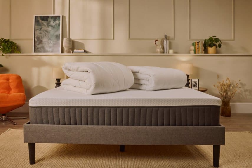 Frau sitzt auf einem Bett und streckt sich, Schlafzimmer mit Regalen und Dekoration im Hintergrund.