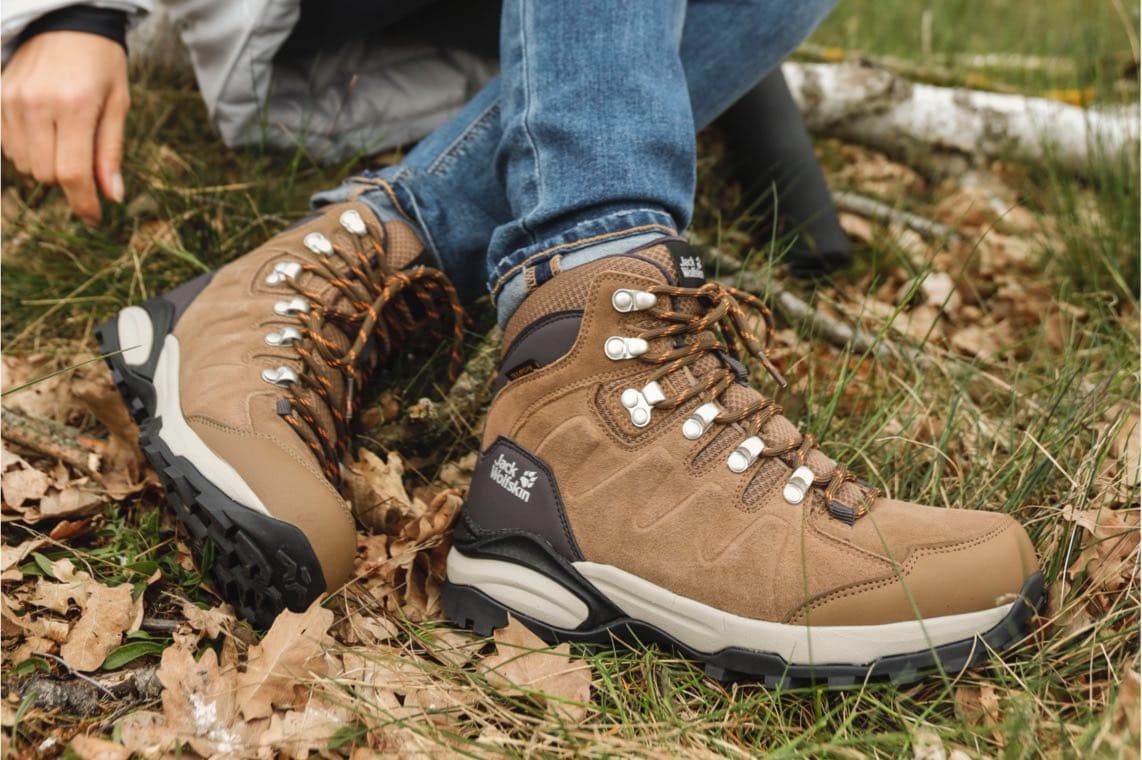 Person sitzt im Gras und trägt braune Wanderschuhe von Jack Wolfskin