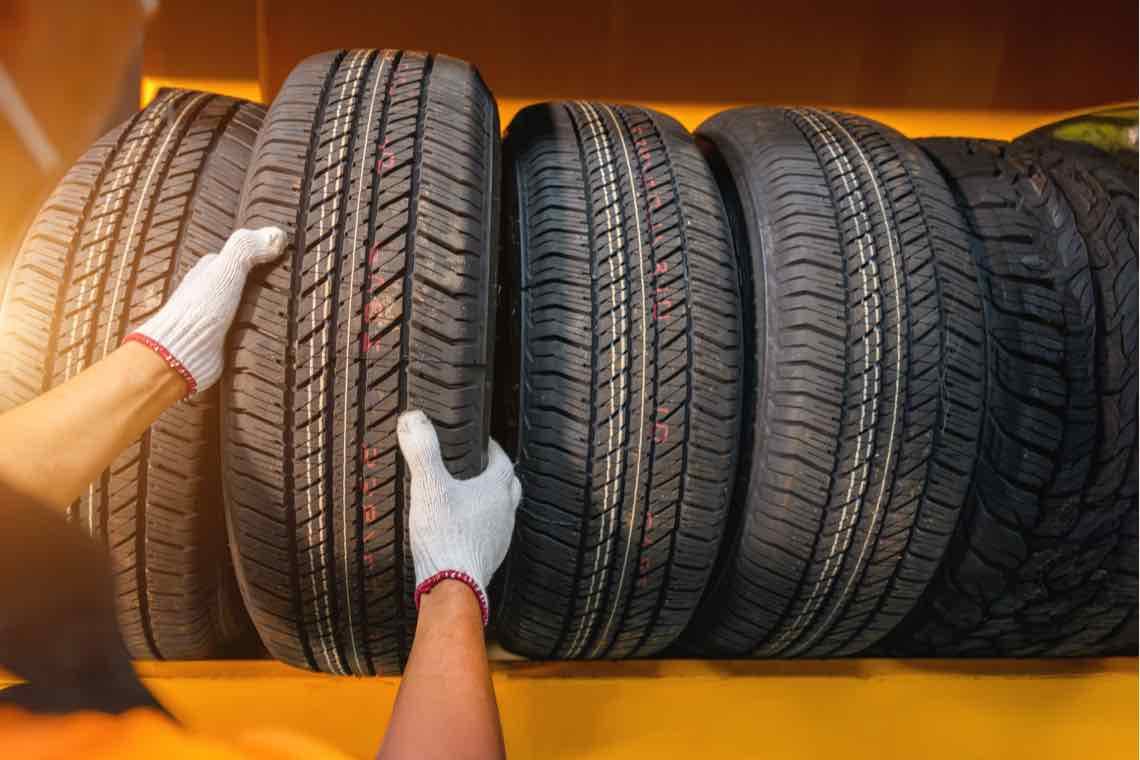 Person mit weißen Handschuhen ordnet mehrere Autoreifen in einer Reihe.