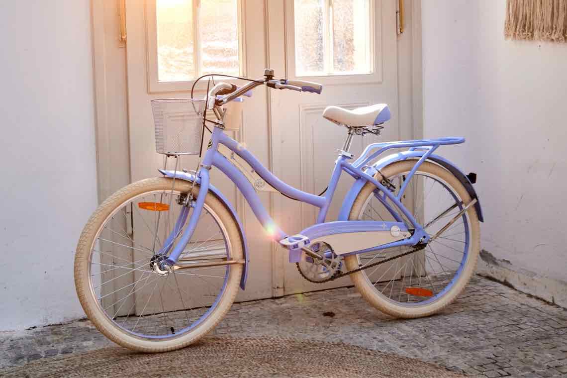 Lila Fahrrad mit Korb steht vor einer Tür, Sonnenstrahlen durch das Fenster.