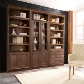 Großes Bücherregal mit Dekorationen und Büchern in einem gemütlichen Raum mit Sessel und Teppich.