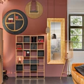 Modernes Wohnzimmer mit Bücherregal, großem Spiegel und dekorativen Wandobjekten vor roter Wand.