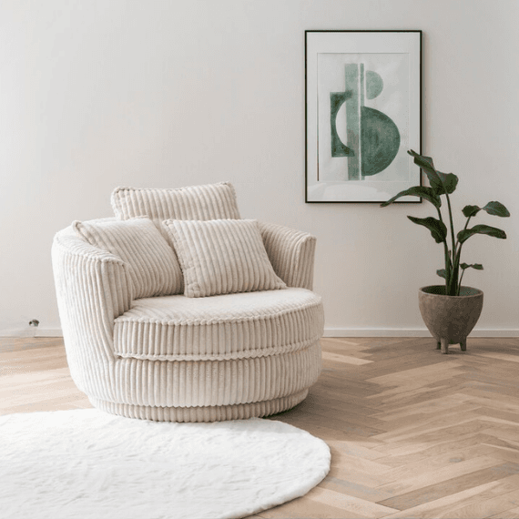 Beiger Sessel mit zwei Kissen auf hellem Holzboden, daneben Pflanze und abstrakte Wandkunst.