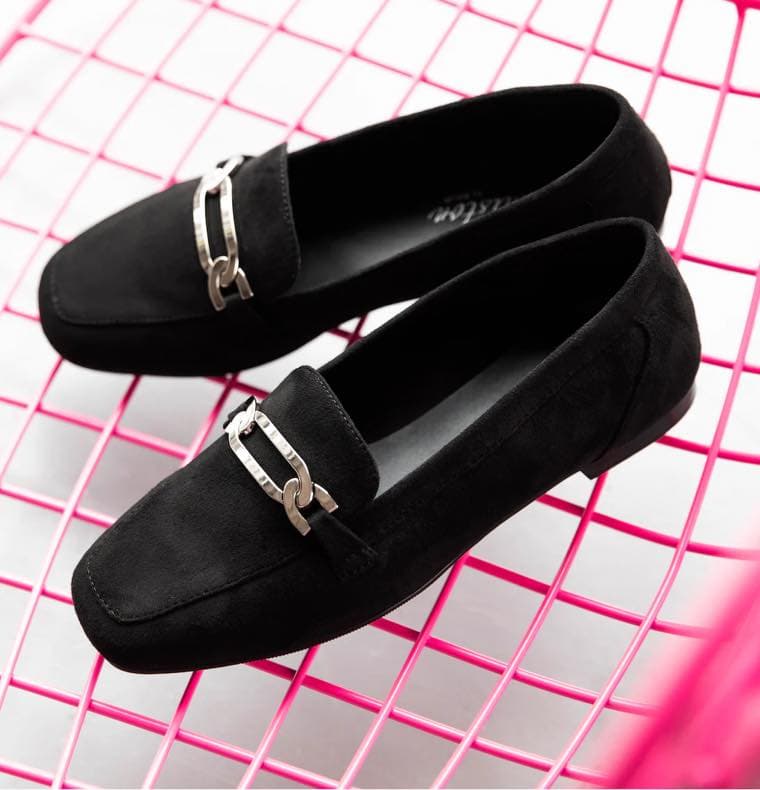 Schwarze Loafer mit silberner Schnalle auf pinkem Gitterdisplay