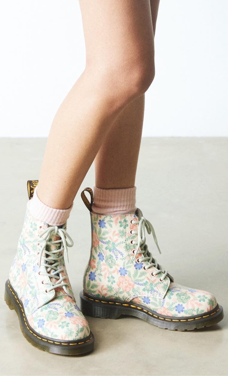 Beine mit rosa Socken und floralen Schnürstiefeln auf grauem Boden.