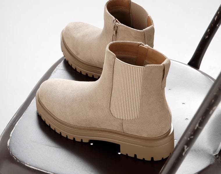 Beige Chelsea-Boots mit elastischen Seiteneinsätzen auf einem braunen Stuhl.