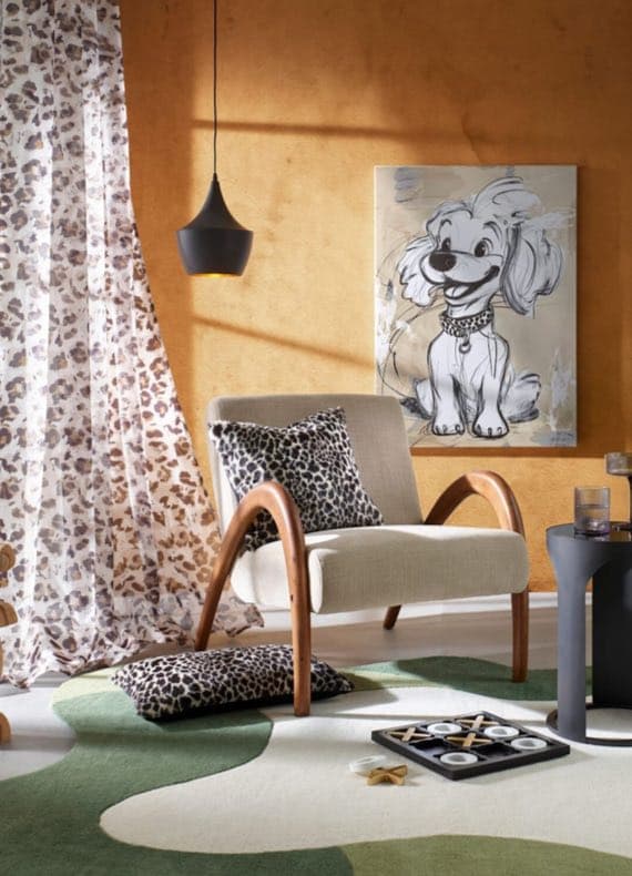 Gemütlicher Raum mit Stuhl, Kissen, Vorhang und Bild eines lächelnden Hundes an der Wand.