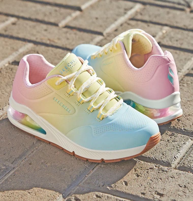 Pastellfarbene Sneaker in Gelb, Rosa und Blau mit sichtbarer Luftsohle stehen auf einem gepflasterten Boden