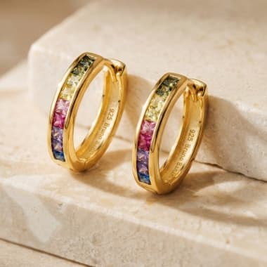 Goldfarbene Creolen mit bunt schimmernden Steinen in Reihe, stehend auf hellen Steinstufen