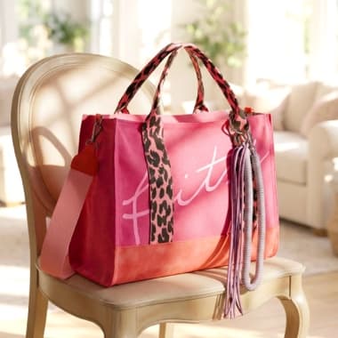 Rosa und orangefarbene Schultertasche mit Leopardenriemen und Fransenanhänger liegt auf einem hellen Stuhl im Wohnzimmer