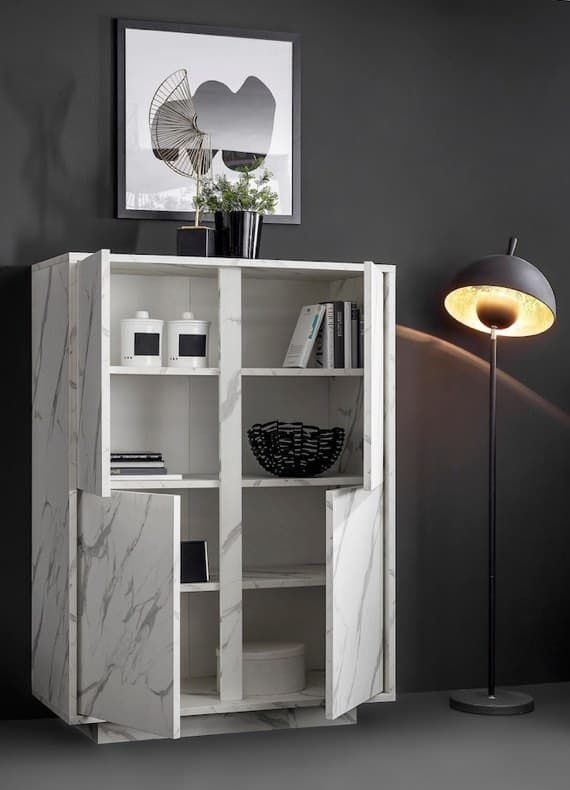 Offener Hochschrank mit Fächern, Deko und Büchern vor dunkler Wand, daneben Stehlampe und gerahmtes Bild an der Wand