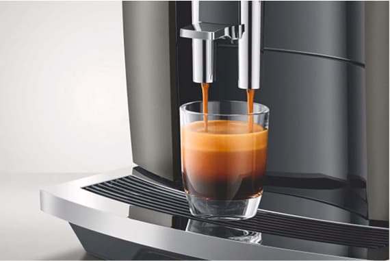 Kaffeevollautomat lässt frischen Espresso mit Crema in ein Glas unter dem Doppelauslauf laufen