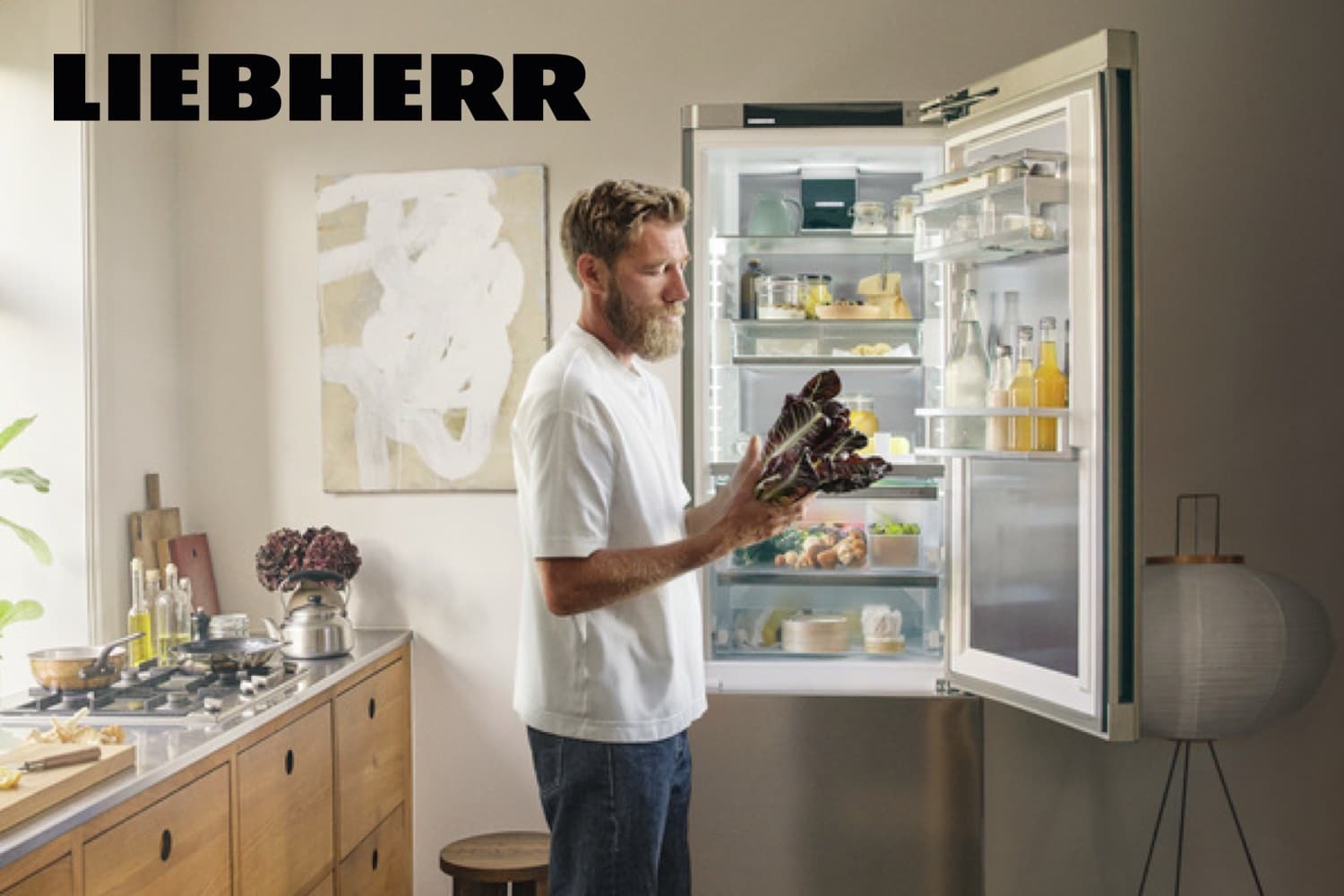 Liebherr – Person steht in moderner Küche vor offenem Kühlschrank und hält frischen Salat in den Händen