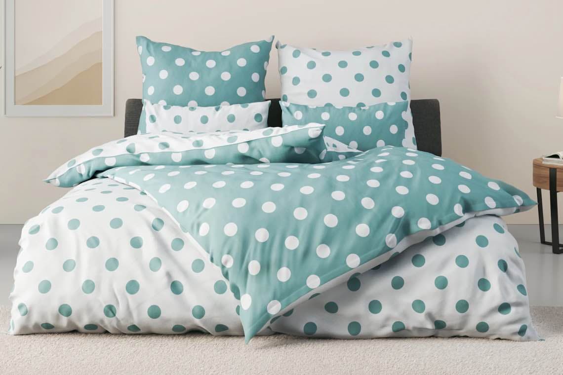 Bett mit Wende-Bettwäsche in Weiß und Türkis, beide Seiten mit großen Punkten, mehrere passende Kissen aufgestellt