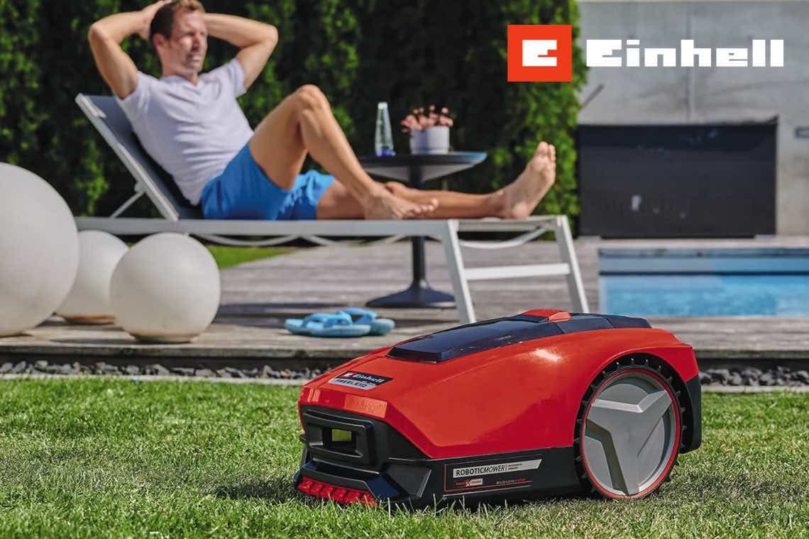 Einhell – roter Mähroboter fährt über Rasen, im Hintergrund entspannt eine Person auf einer Liege am Pool