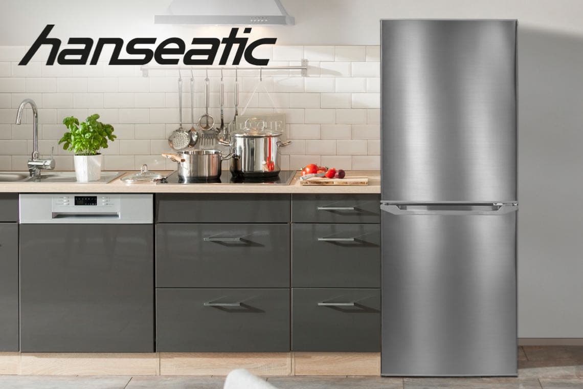 hanseatic – Kühlschrank mit Gefrierteil steht neben moderner Küchenzeile mit Herd, Töpfen und Schneidebrett mit Gemüse