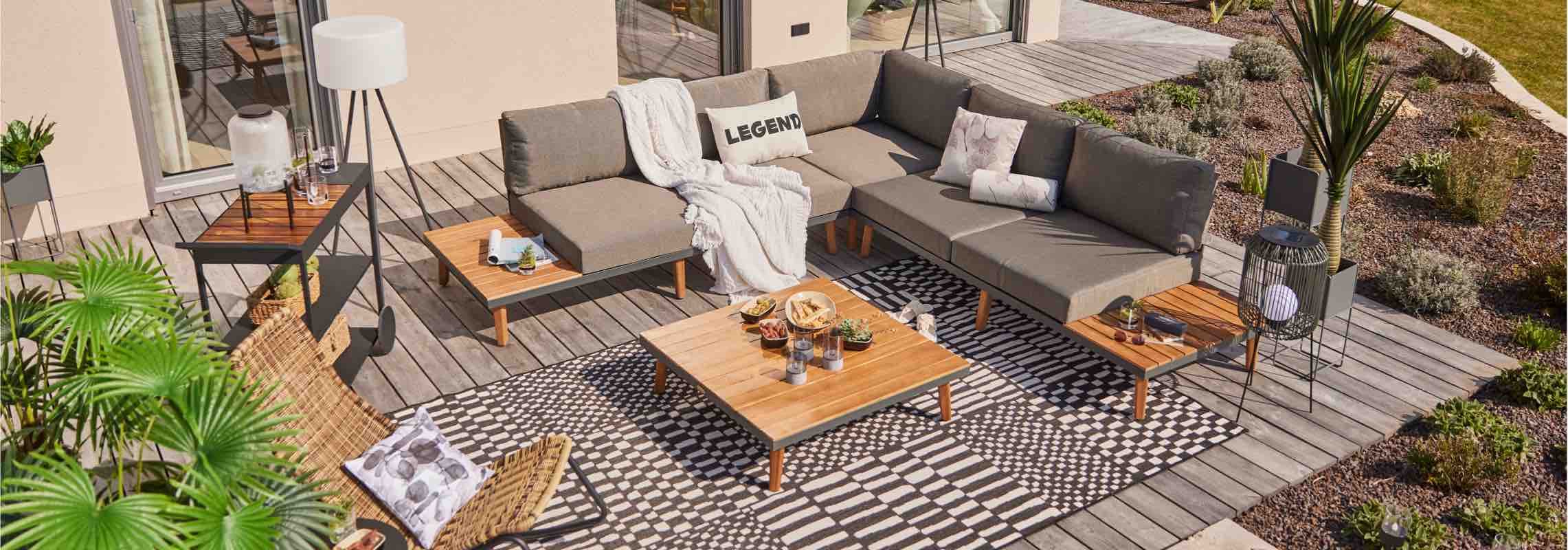 Große Eck-Lounge auf Holzterrasse mit Tischen, Teppich, Pflanzen und Deko für eine gemütliche Sitzecke im Garten