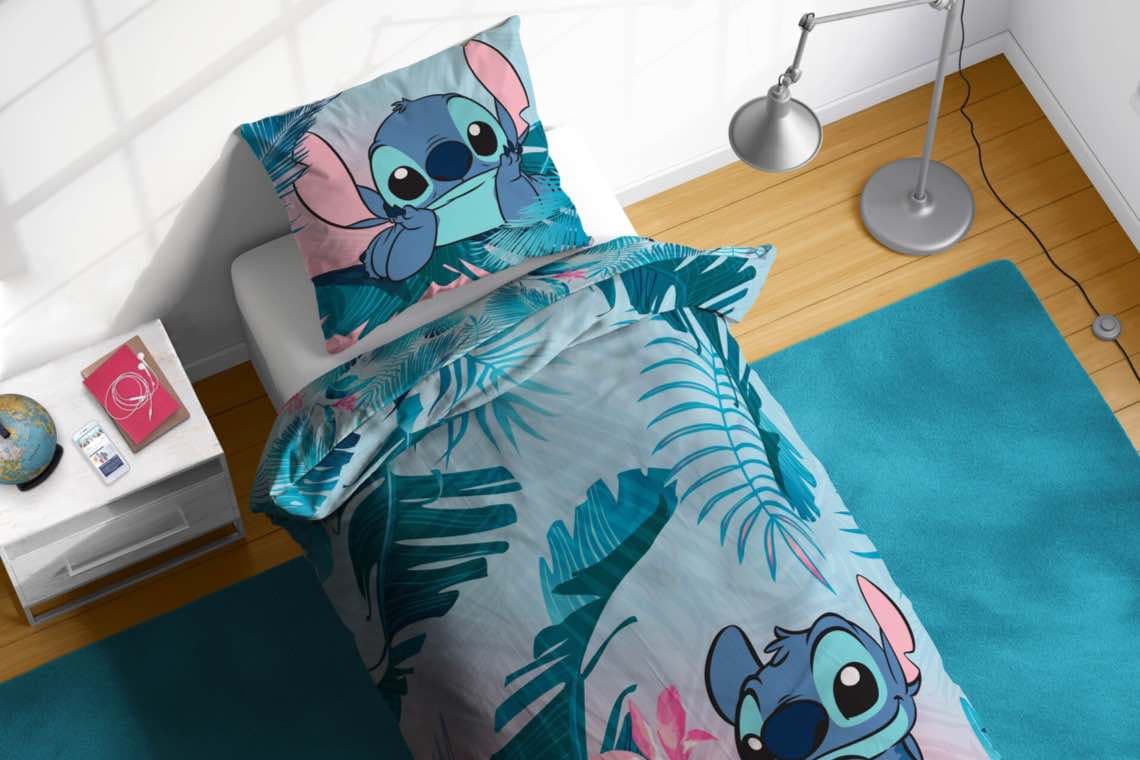 Einzelbett mit Stitch-Bettwäsche im Palmenmotiv, Nachttisch mit Globus und Buch, daneben Stehlampe und türkisfarbener Teppich