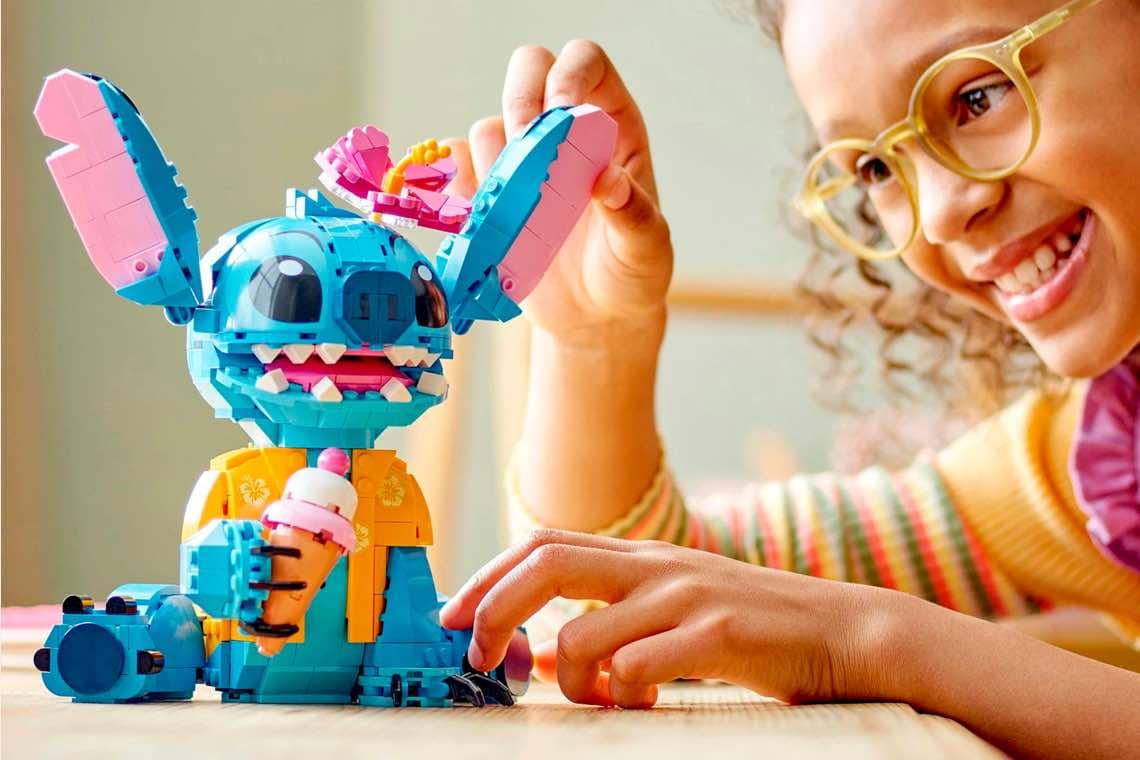 Kind spielt am Tisch mit buntem baubarem Alien-Spielzeug, richtet dessen Ohren und hält eine Hand an den Fuß