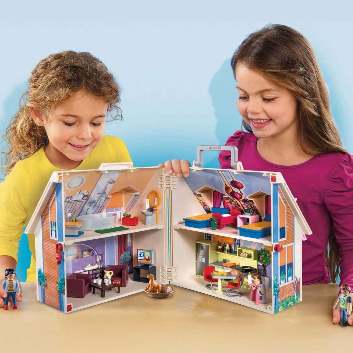 Zwei Kinder spielen am Tisch mit geöffnetem Puppenhaus, das bunte eingerichtete Zimmer auf zwei Etagen zeigt