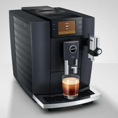Schwarzer Kaffeevollautomat mit Display brüht einen frisch geschichteten Kaffee in ein Glas auf der Tropfschale