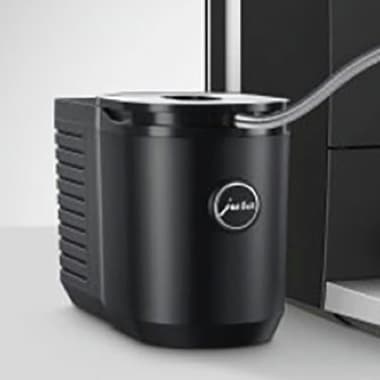 Schwarzer Milchkühler mit Schlauchanschluss steht neben einer Kaffeemaschine