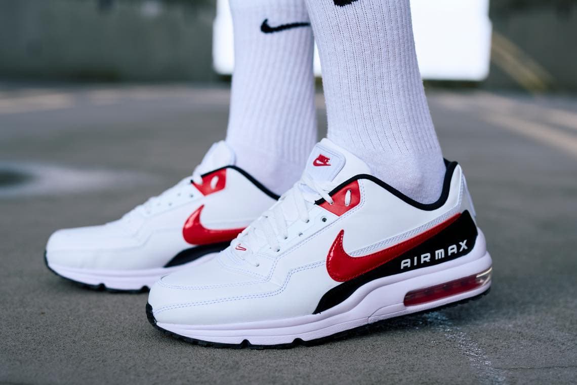Air Max Sneaker mit rotem Swoosh – Person steht in weißen Sportsocken auf grauem Boden