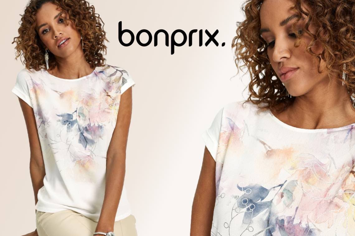 bonprix – Frau mit lockigem Haar trägt helles T-Shirt mit buntem, abstraktem Blumenprint und kurzen Ärmeln