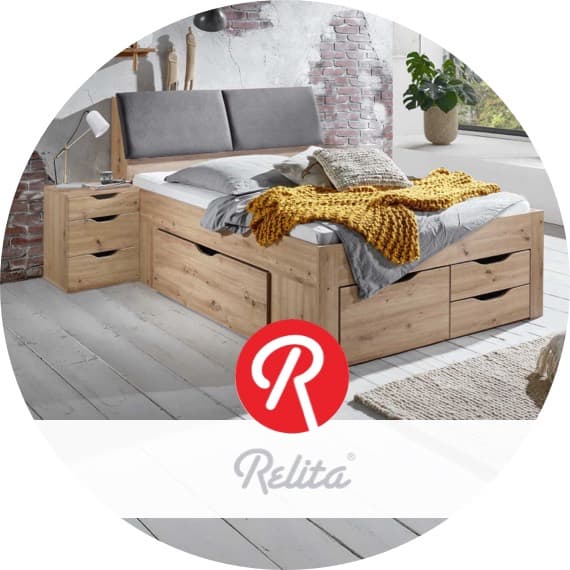 Relita Logo vor Schlafzimmer mit Doppelbett und Schubladen, Nachttisch und Decke in hellem Raum mit Backsteinwand