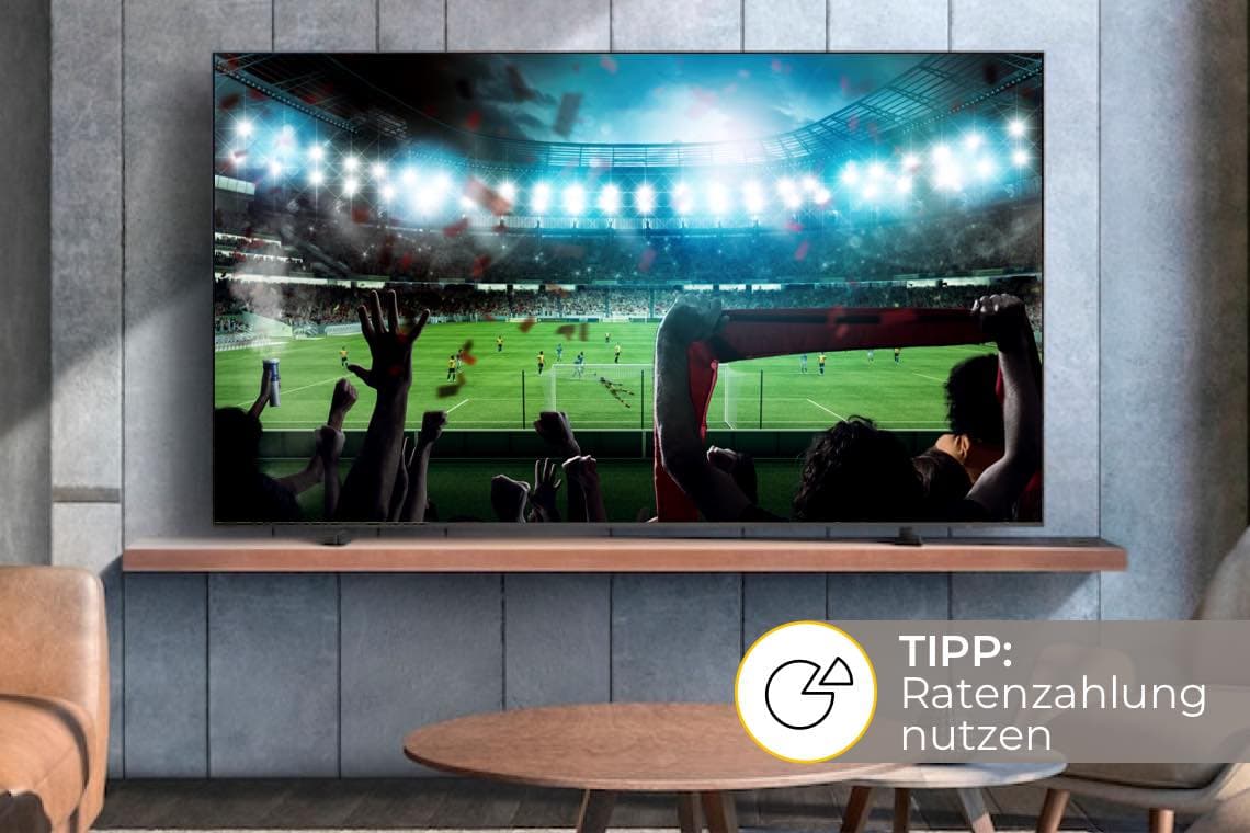 TIPP: Ratenzahlung nutzen – großer Fernseher zeigt Fußballstadion mit jubelnden Fans im modernen Wohnzimmer
