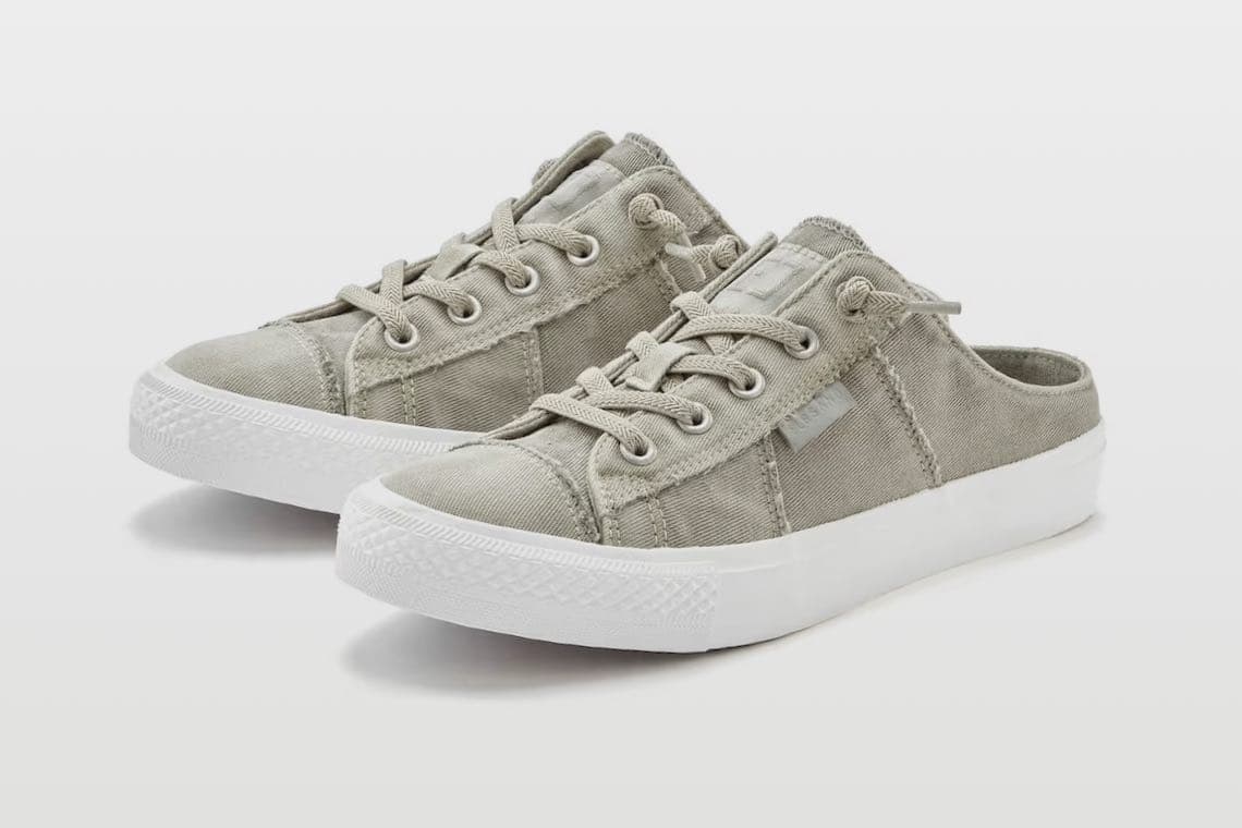 Beige Sneaker-Pantoletten mit Schnürung und weißer Sohle, seitlich versetzt vor weißem Hintergrund platziert