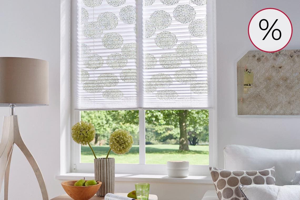 % Zeichen – Wohnzimmer mit Fenster und Plissee mit Kreis-Muster, Blick ins Grüne, Deko auf der Fensterbank